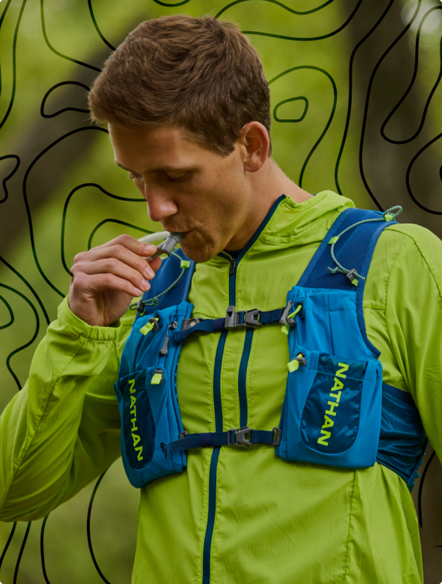 Male runner wearing a Nathan Stealth Jacket while drinking from his Nathan hydration vest