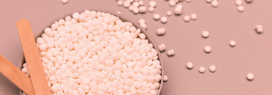 Bowl of white beads on a pink surface with wooden sticks.