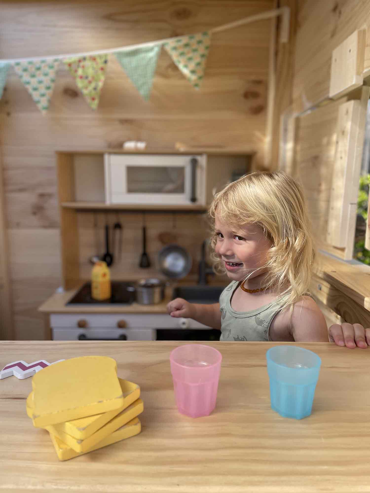 Kids serving up drinks from their wooden cubby house windows