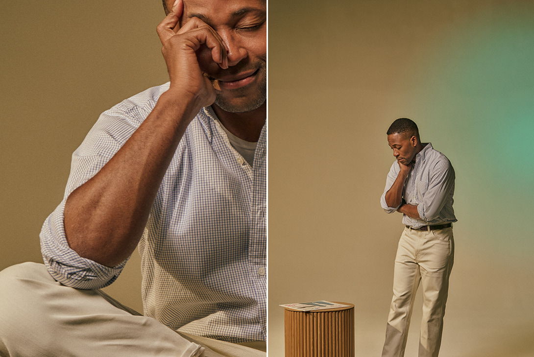 Man in casual attire, looking contemplative, standing next to a wooden stool.