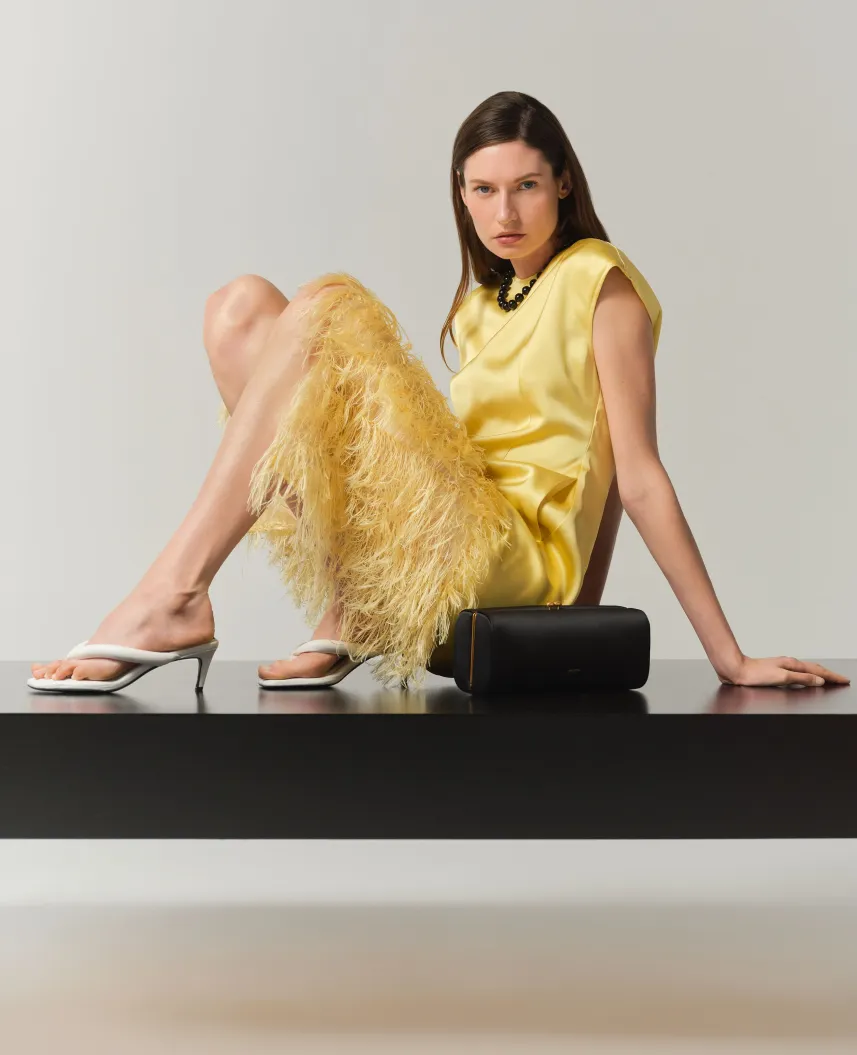 Woman in yellow outfit sitting on a black surface with a handbag.