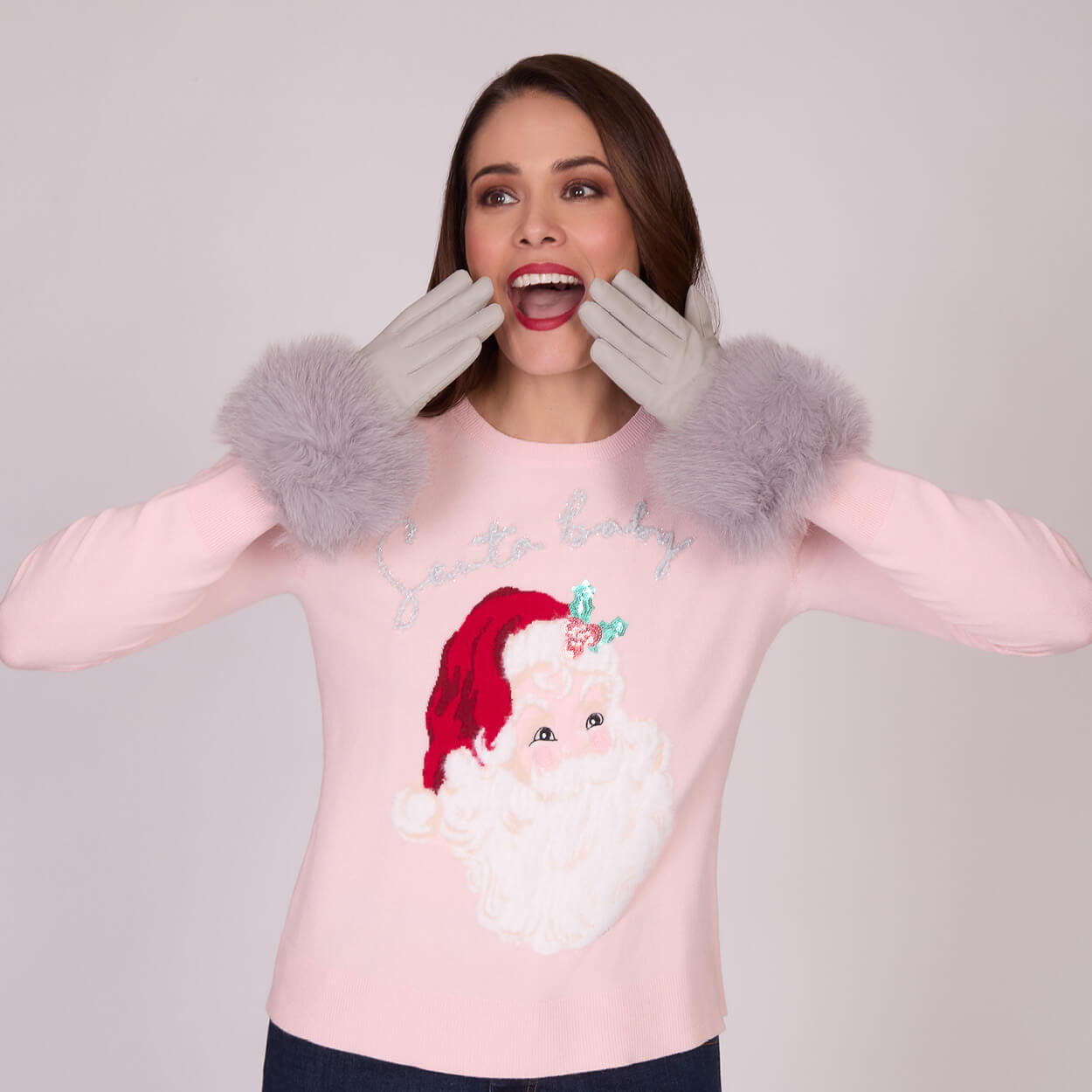 Woman in a pink sweater with Santa design and gray fluffy gloves.