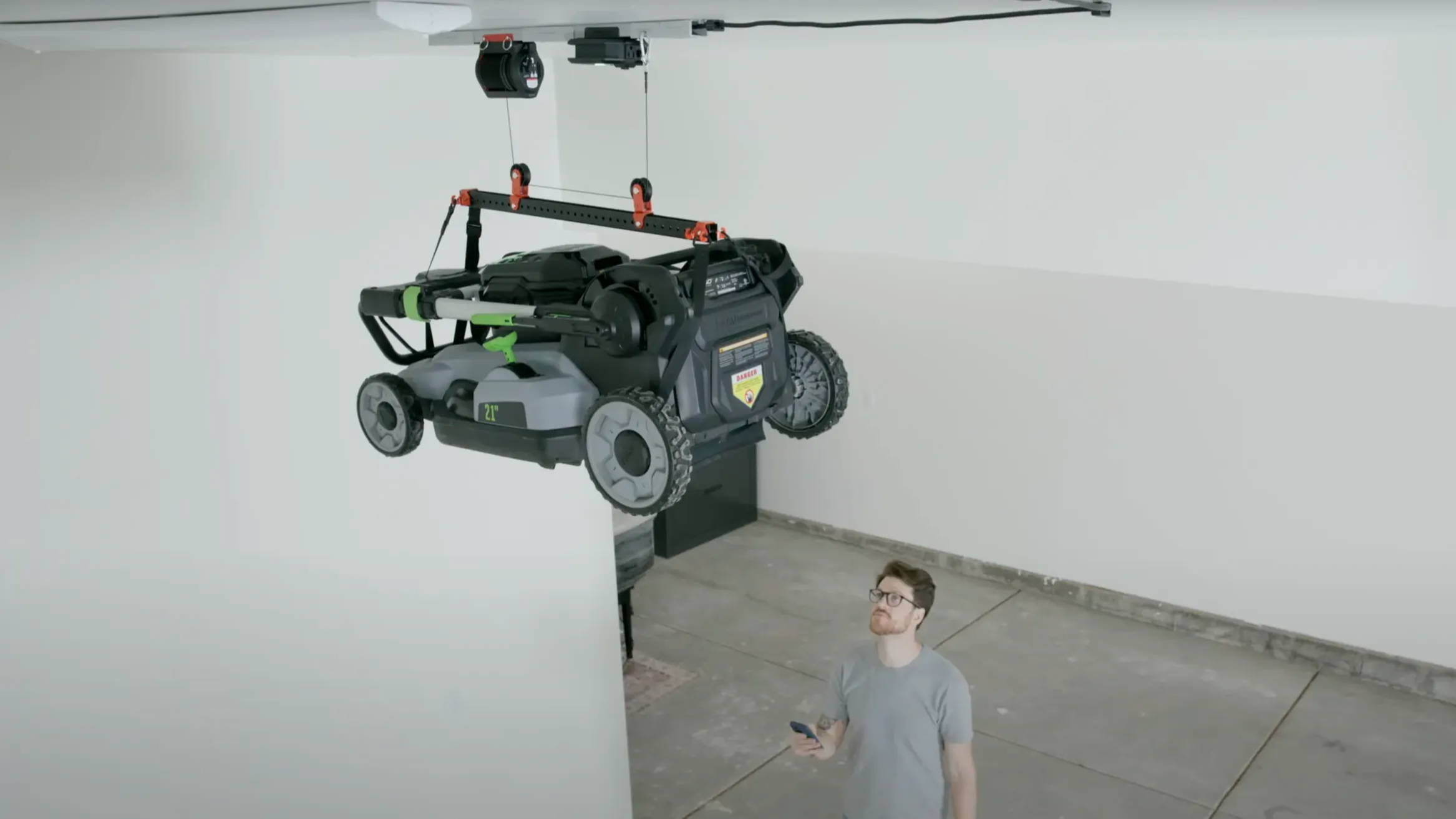 Man standing under the Universal Lifter holding a lawn mower