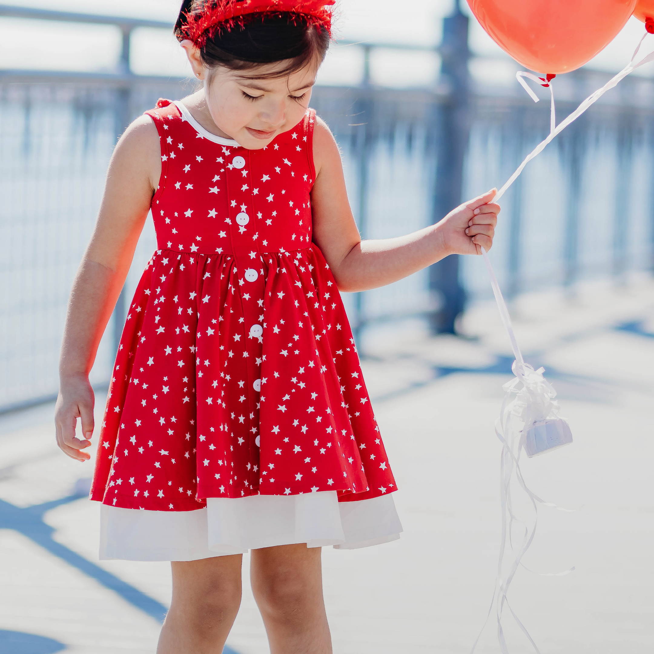 girl in red star patterned dress holding red balloons
