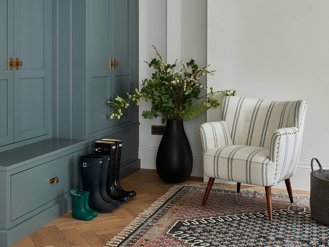 Family home mudroom design by McClarke Bespoke Kitchens with mid blue cabinetry, brass hardware, wood flooring and cosy furnishings