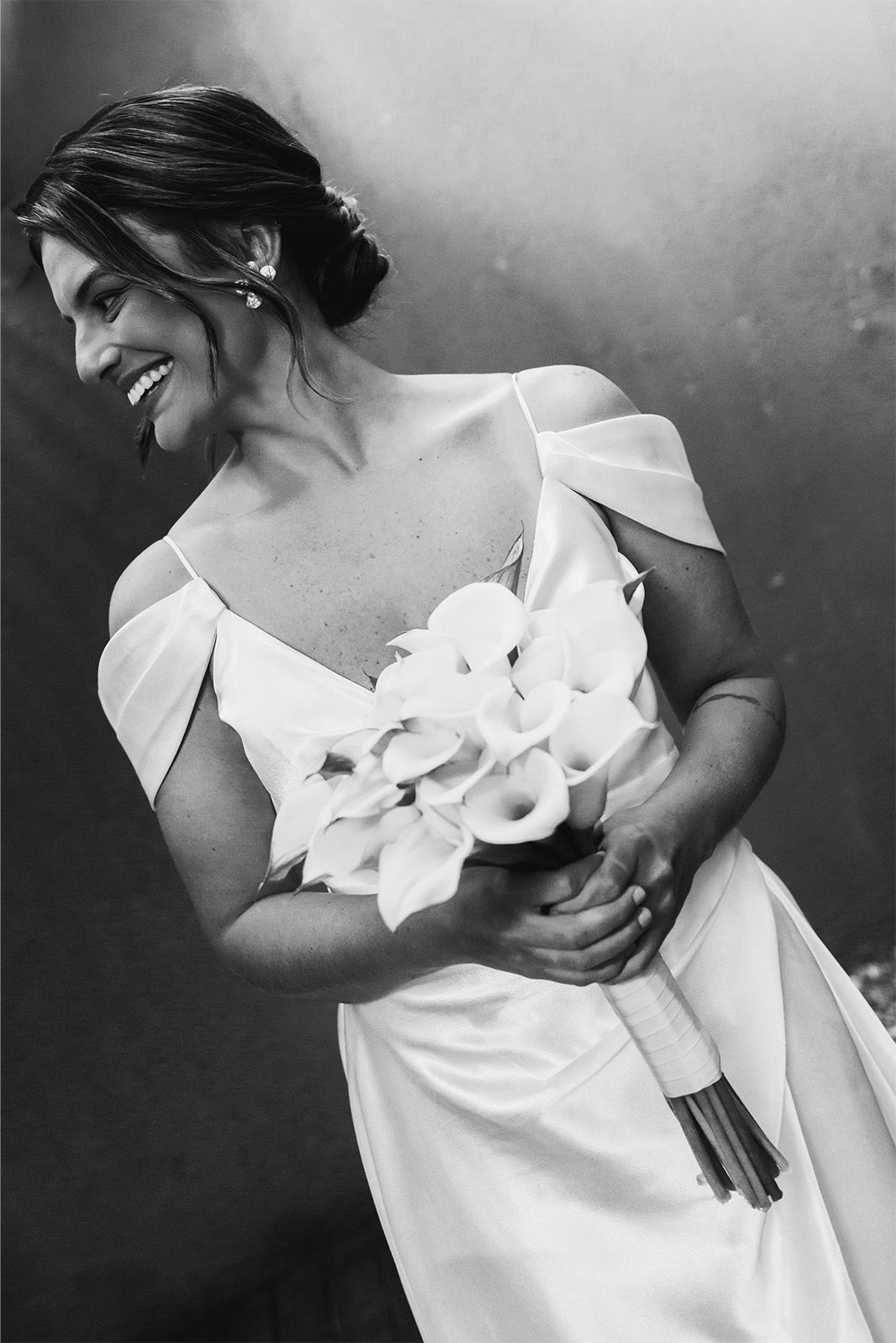 Smiling woman in a wedding dress holding a bouquet of calla lilies.