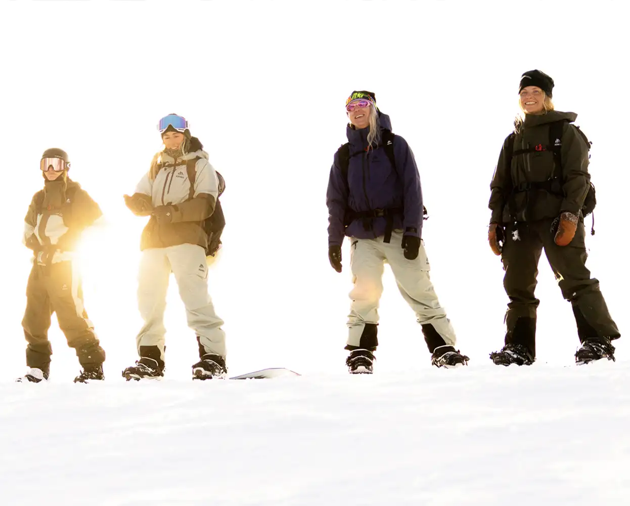 Four people standing on snow, dressed in winter gear, with bright sunlight.