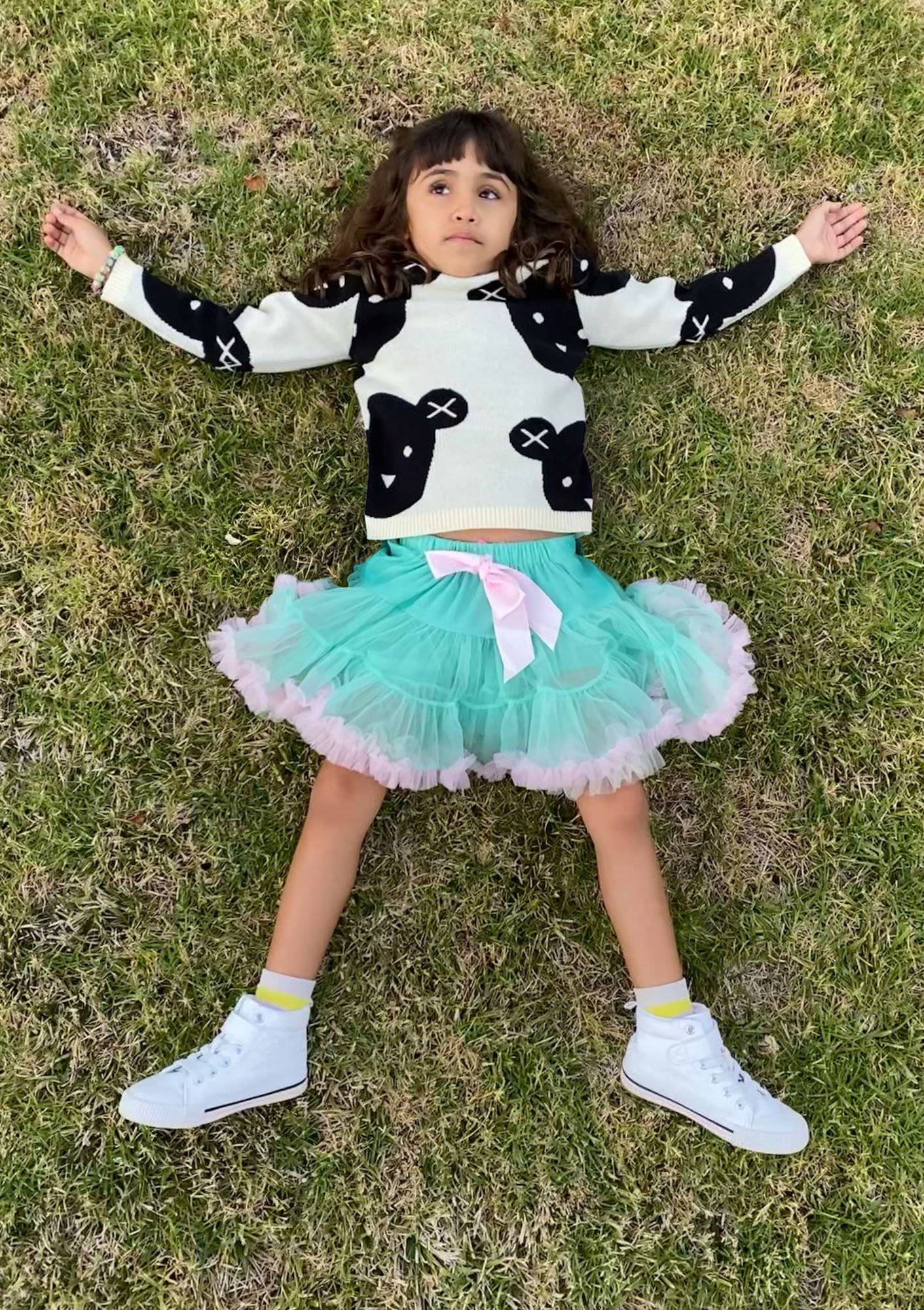 Young girl laying down in the grass in a tulle skirt and graphic tee