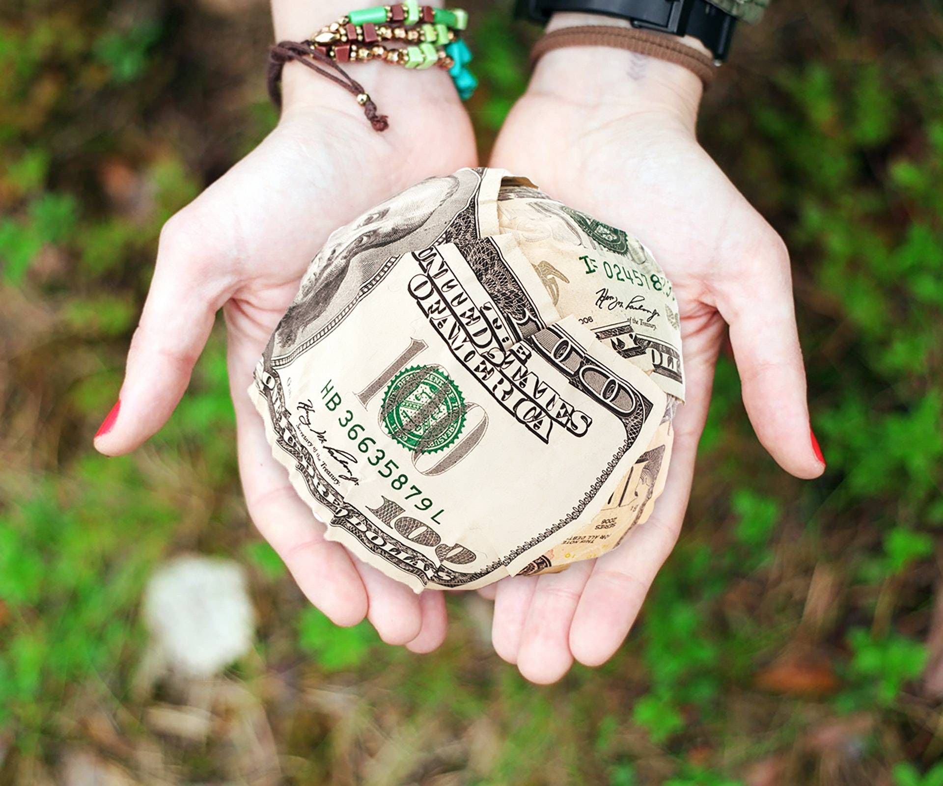 Hands holding a ball of 100 dollar bills