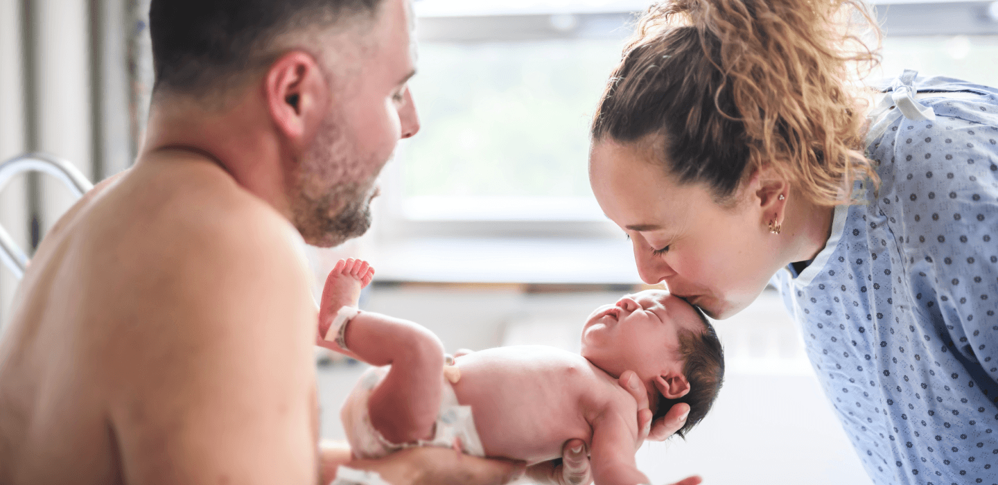 Parents admiring their newborn baby in a hospital setting.