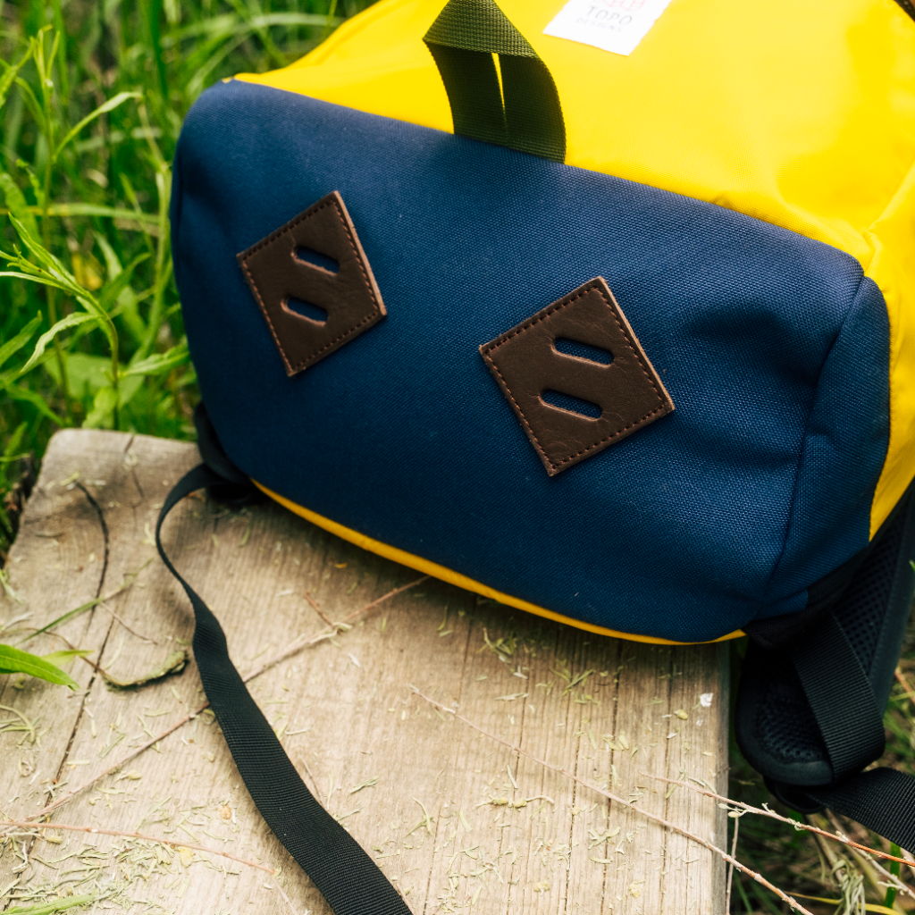 A yellow and blue backpack resting on a wooden surface in grass.