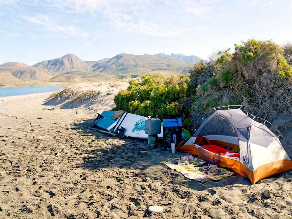 paddleboard camping on a remote beach with mountains in the background