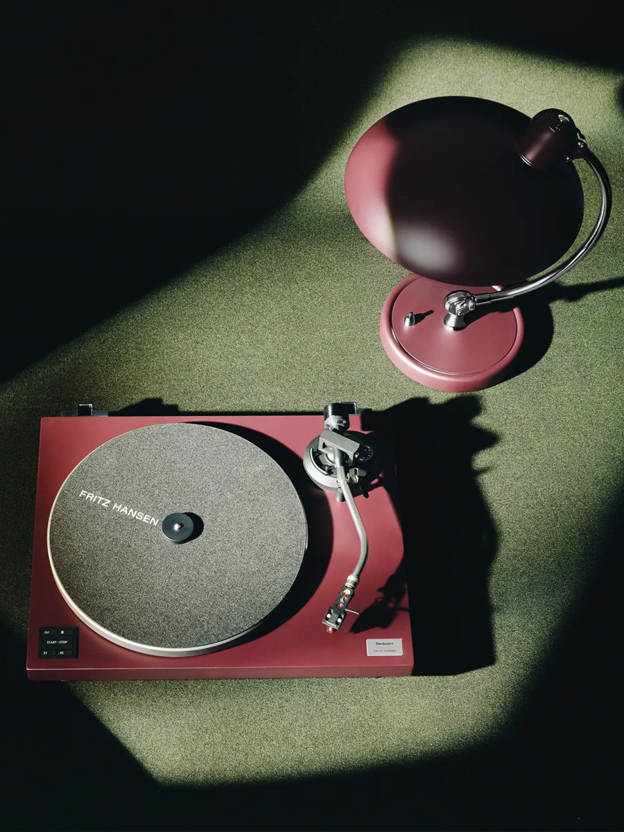 A red Technics turntable next to a matching a Kaiser Idell lamp on a green surface.