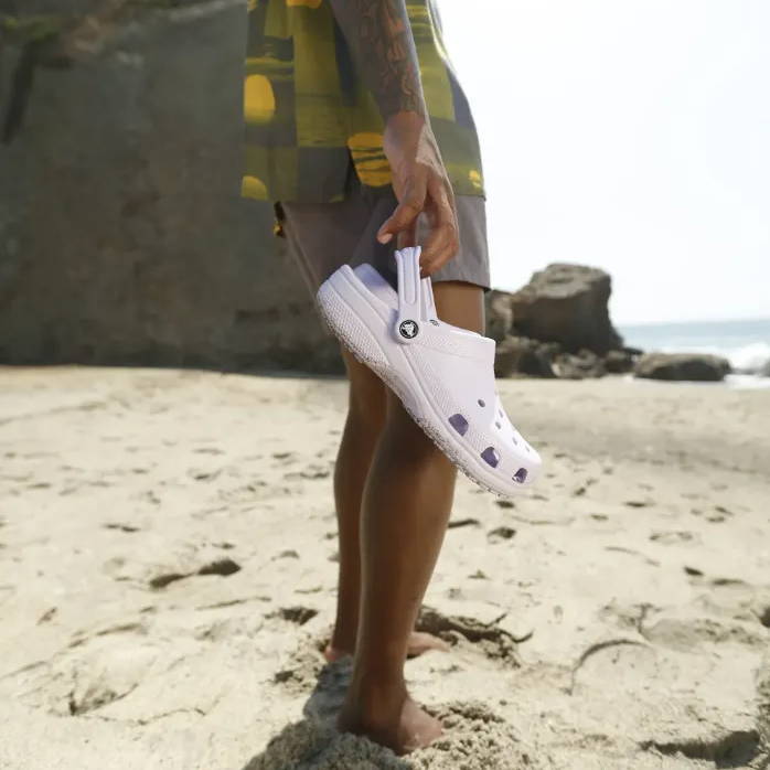 male holding white crocs on beach