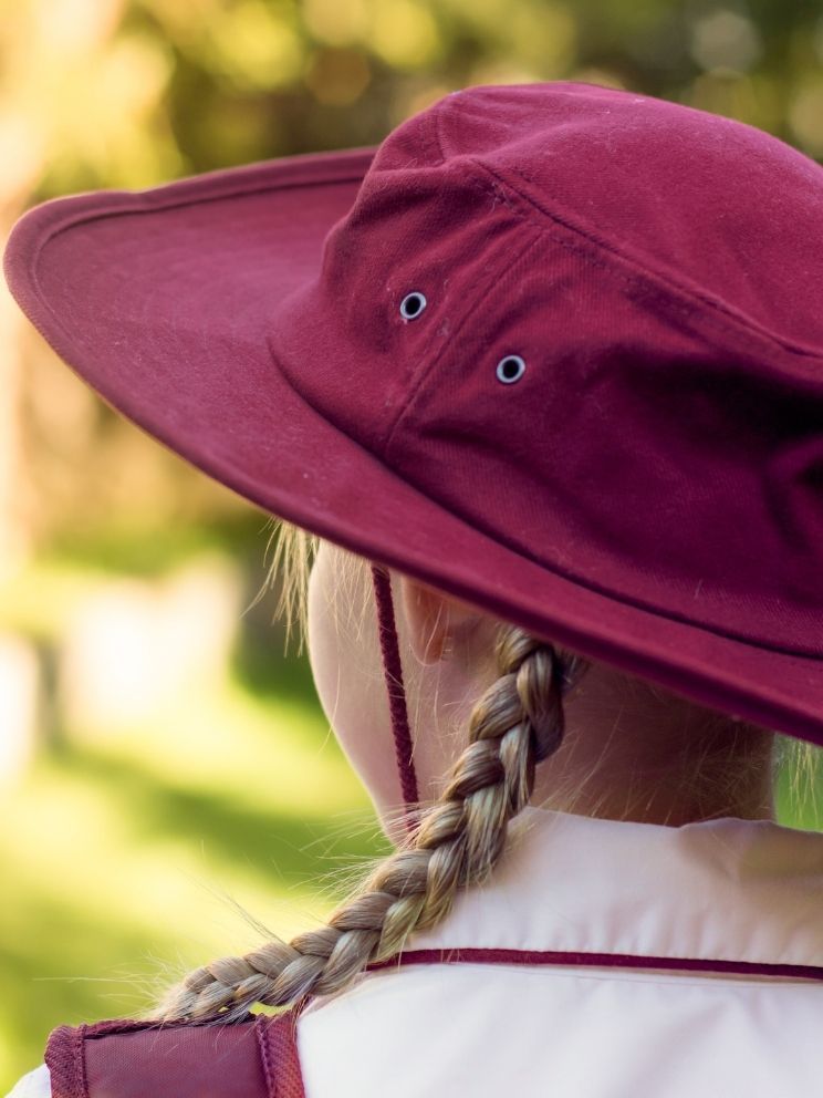 Maroon school hat on student in playground sunlight