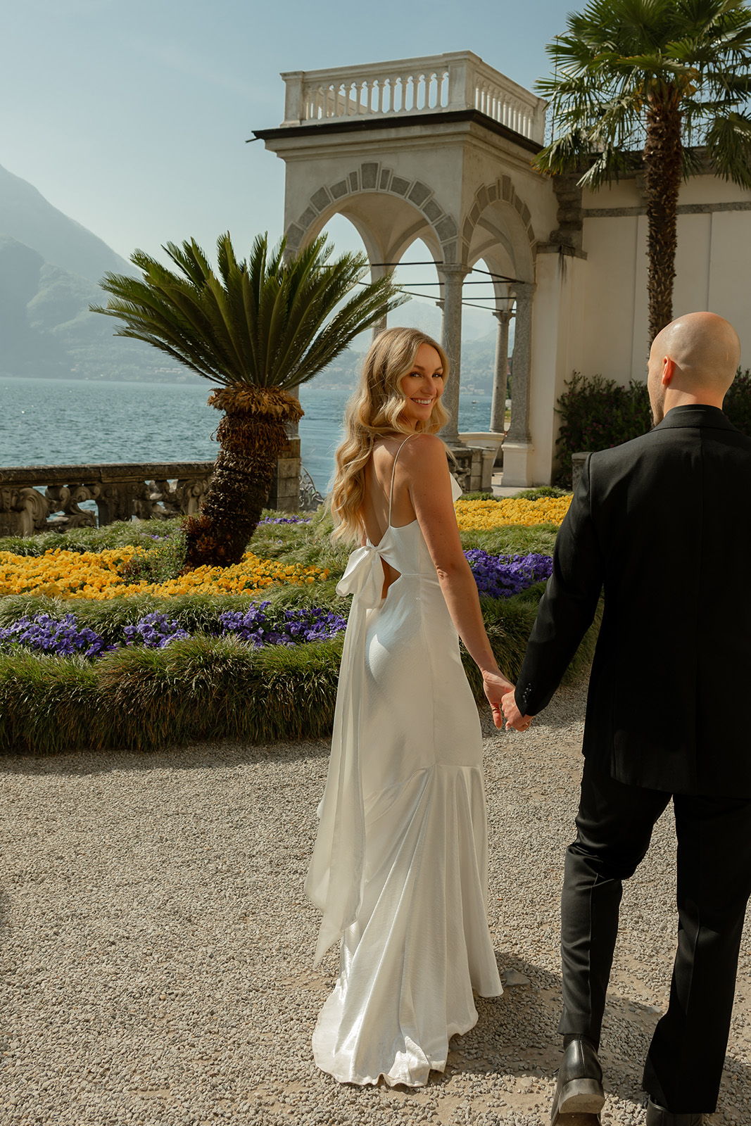 A couple walking hand in hand in a scenic garden setting.