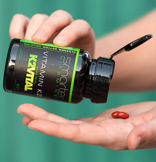 Opened Vitamin K2 bottle in hand, pouring vitamins into other hand.
