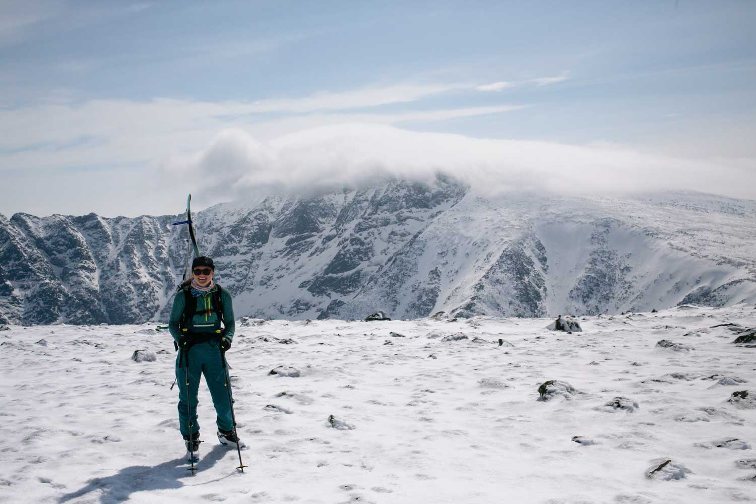 Person standing in snow with mountains in the background under a cloudy sky.