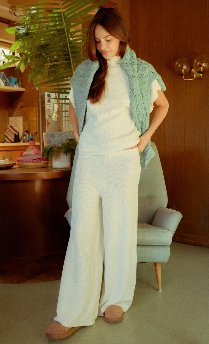Woman in white outfit stands in a cozy indoor setting.