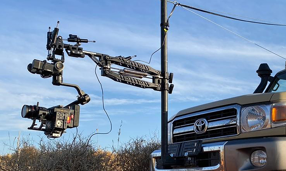 Camera equipment mounted on a pole next to a vehicle.