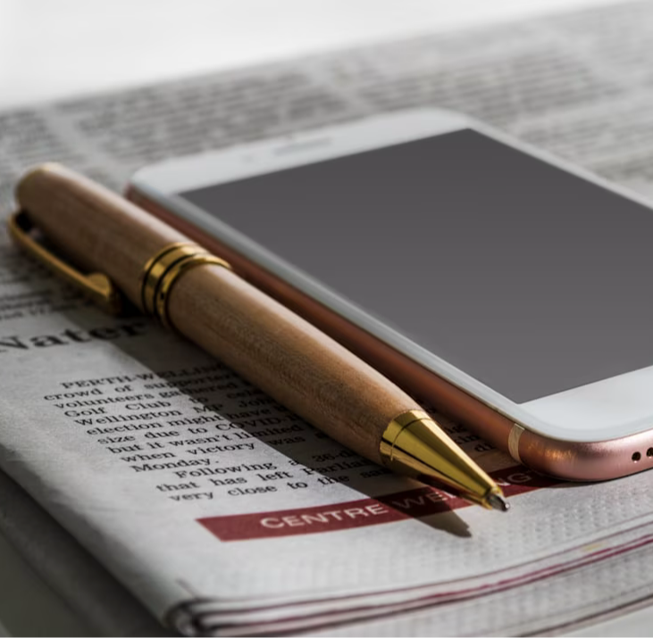a cell phone sitting on top of a newspaper next to a pen