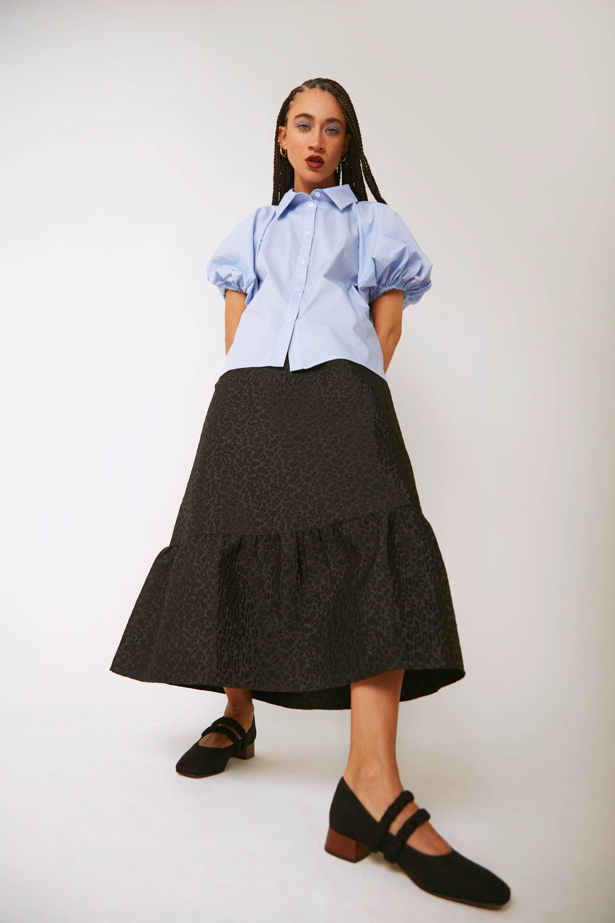Vandrelaar Ruth mary-jane pump in black linen worn by model and styled with a jacquard black midi skirt and a light blue blouse with puff sleeves