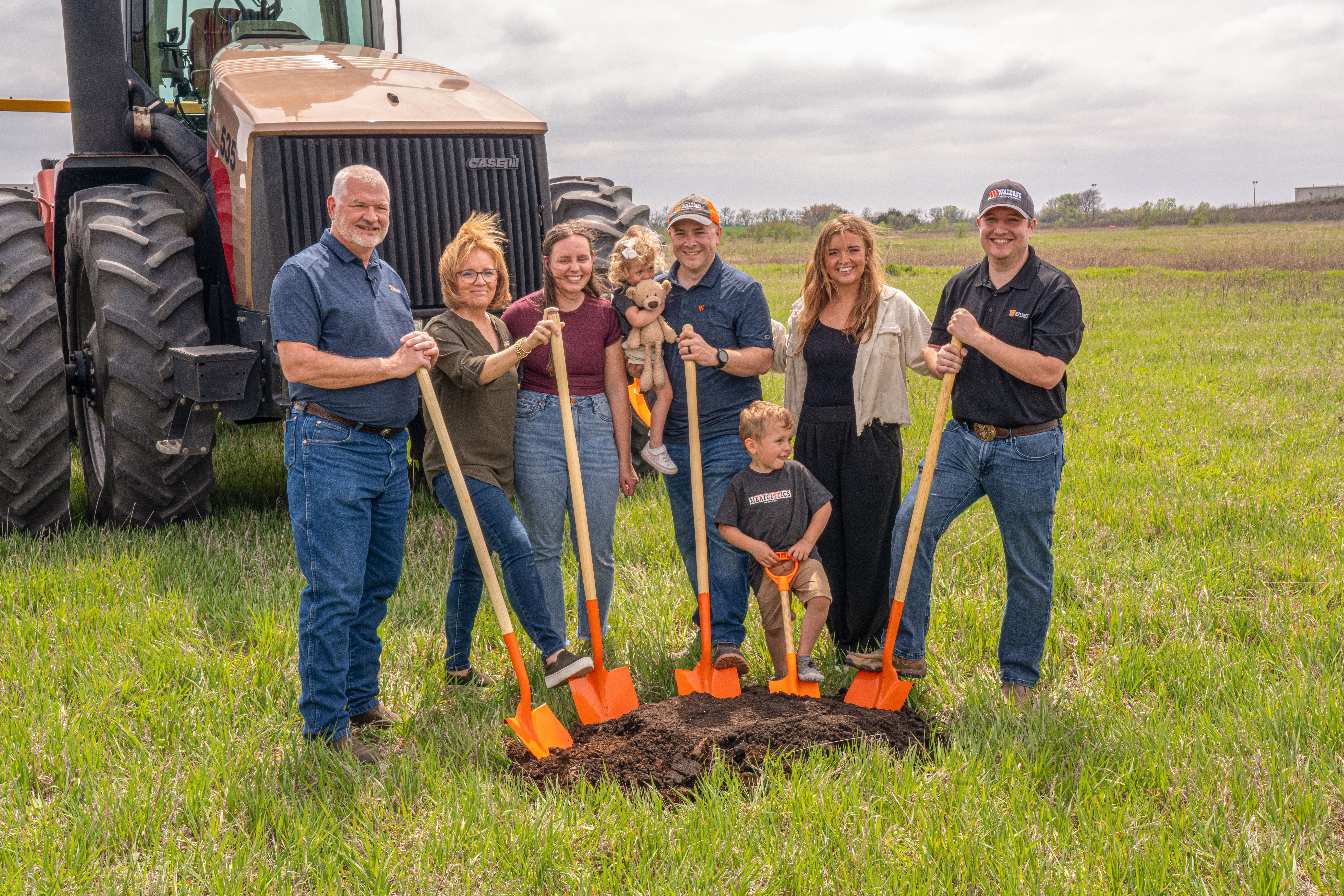 Walton's family with shovels in a field near a tractor.