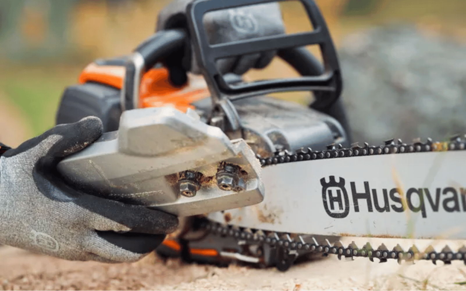 Close-up of a chainsaw with a Husqvarna logo and a glove.