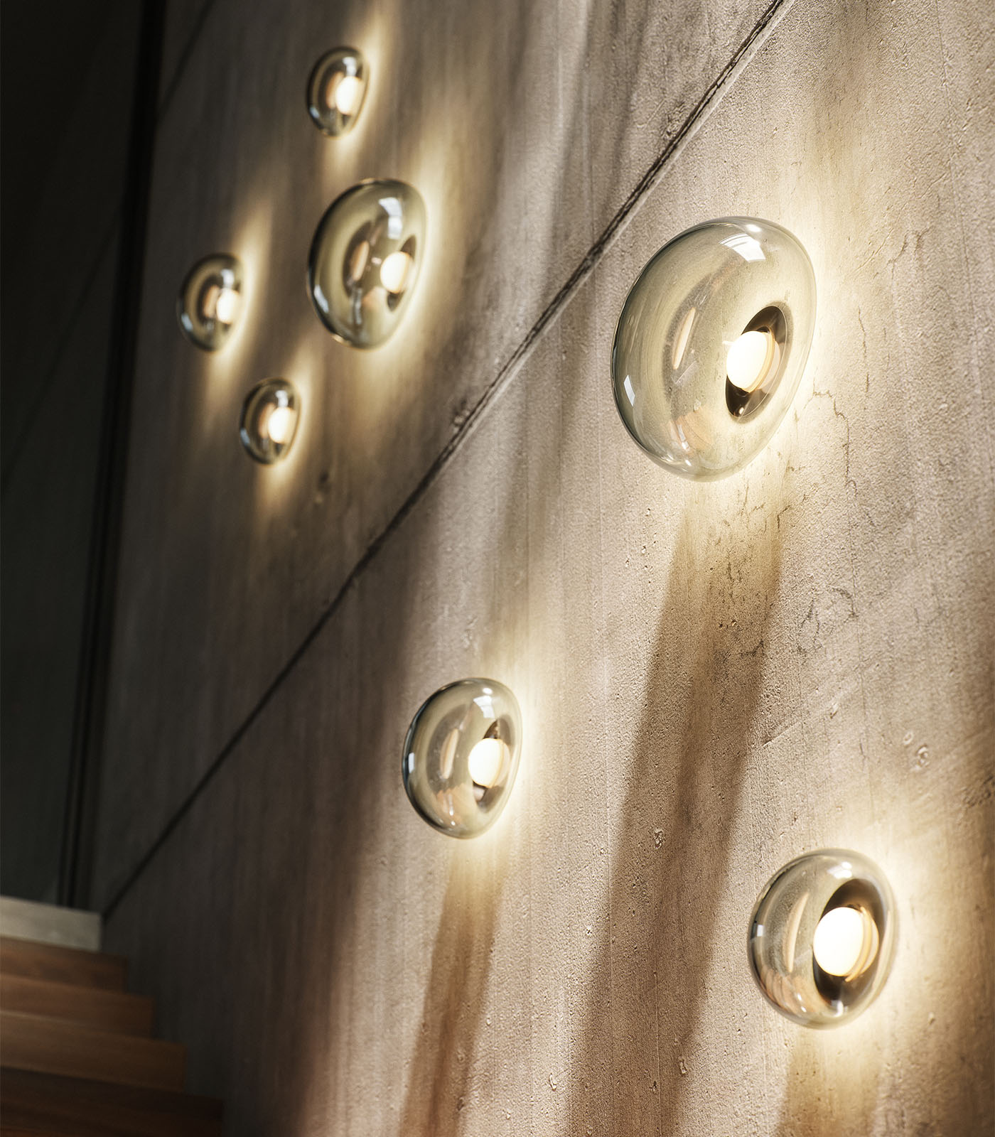 Modern hand blown wall lights illuminating a textured concrete surface.