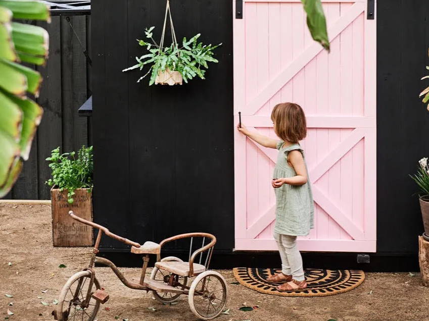 A kid closing a door of a black and pink painted cubby house