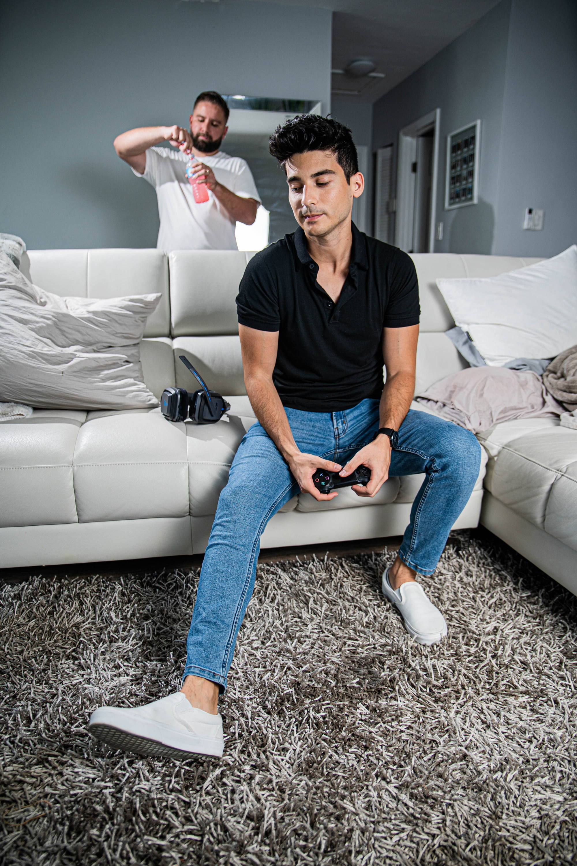 Man playing video games wearing a black polo shirt, white shoes, and jeans for short men from under510.com
