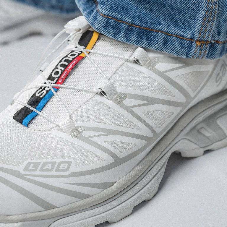 A close-up of white athletic shoes with colorful laces and denim jeans.