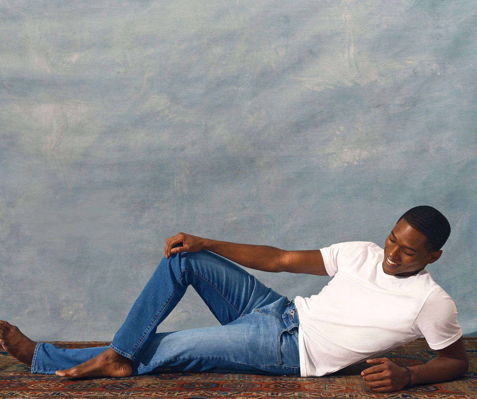 Man in a white shirt and blue jeans lying on a rug.