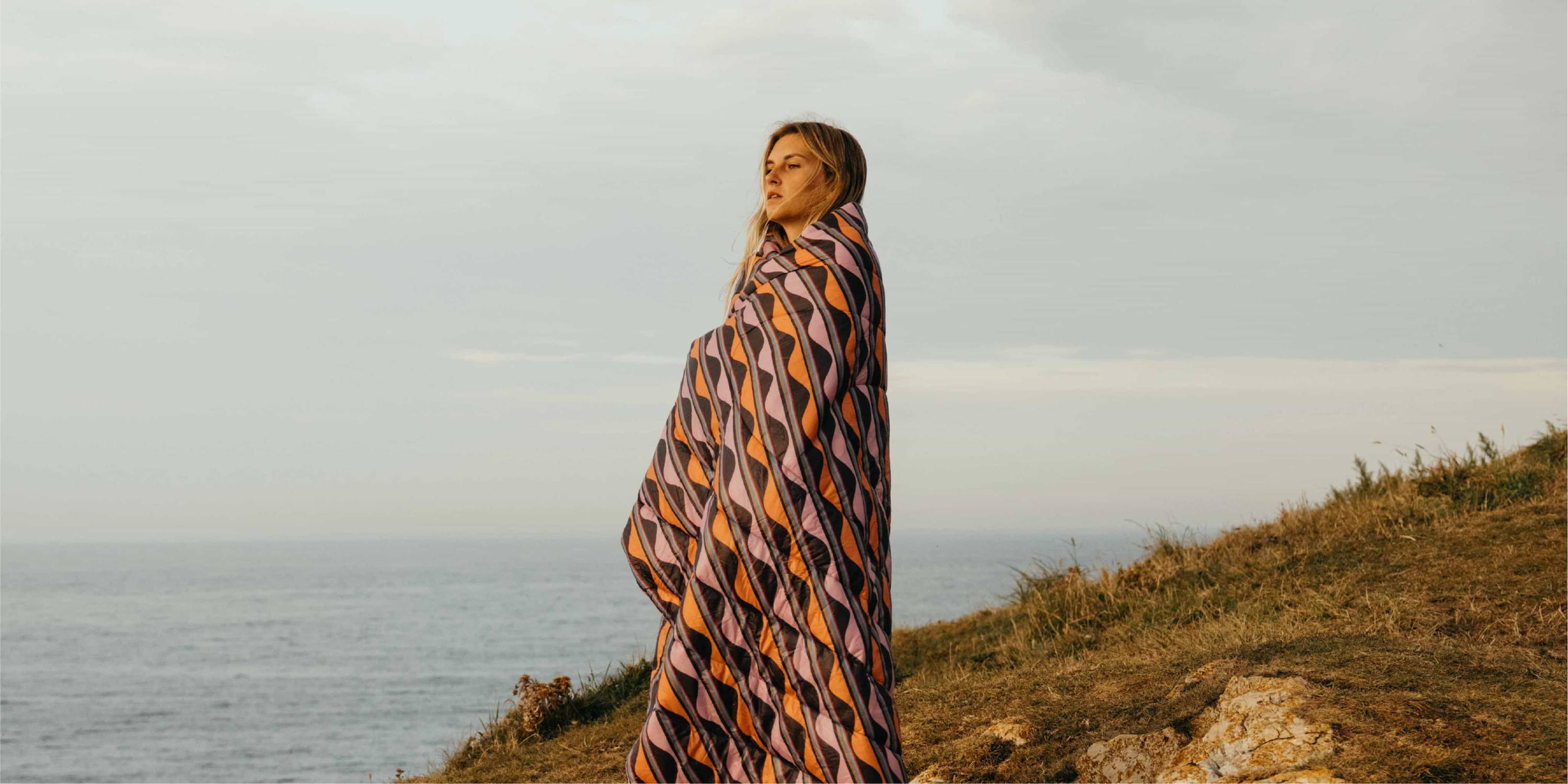 Woman standing on coast wrapped in Original Puffy Blanket
