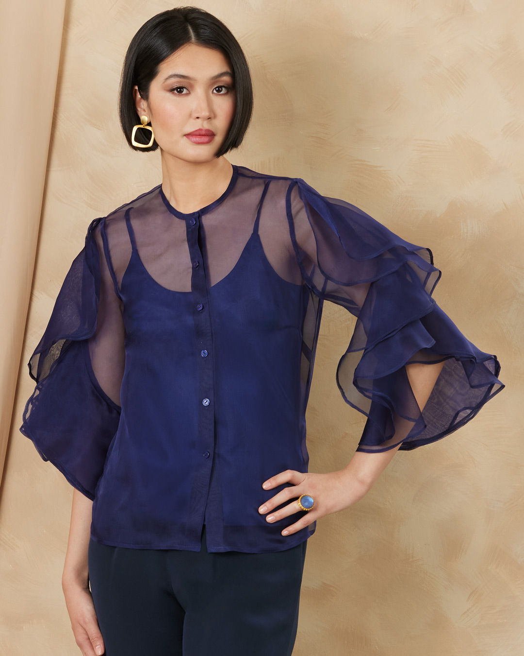 Model wearing a navy blue sheer blouse with ruffled sleeves against a neutral background.