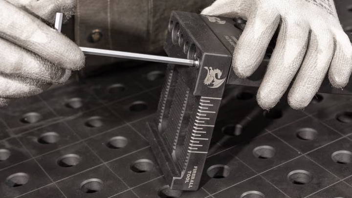 Person using a tool on a metal work surface with holes.