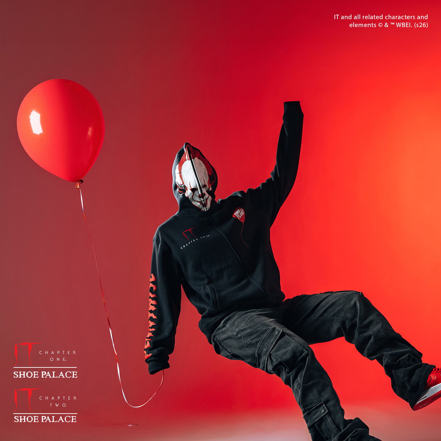 Person in mask holding a red balloon against a red background.