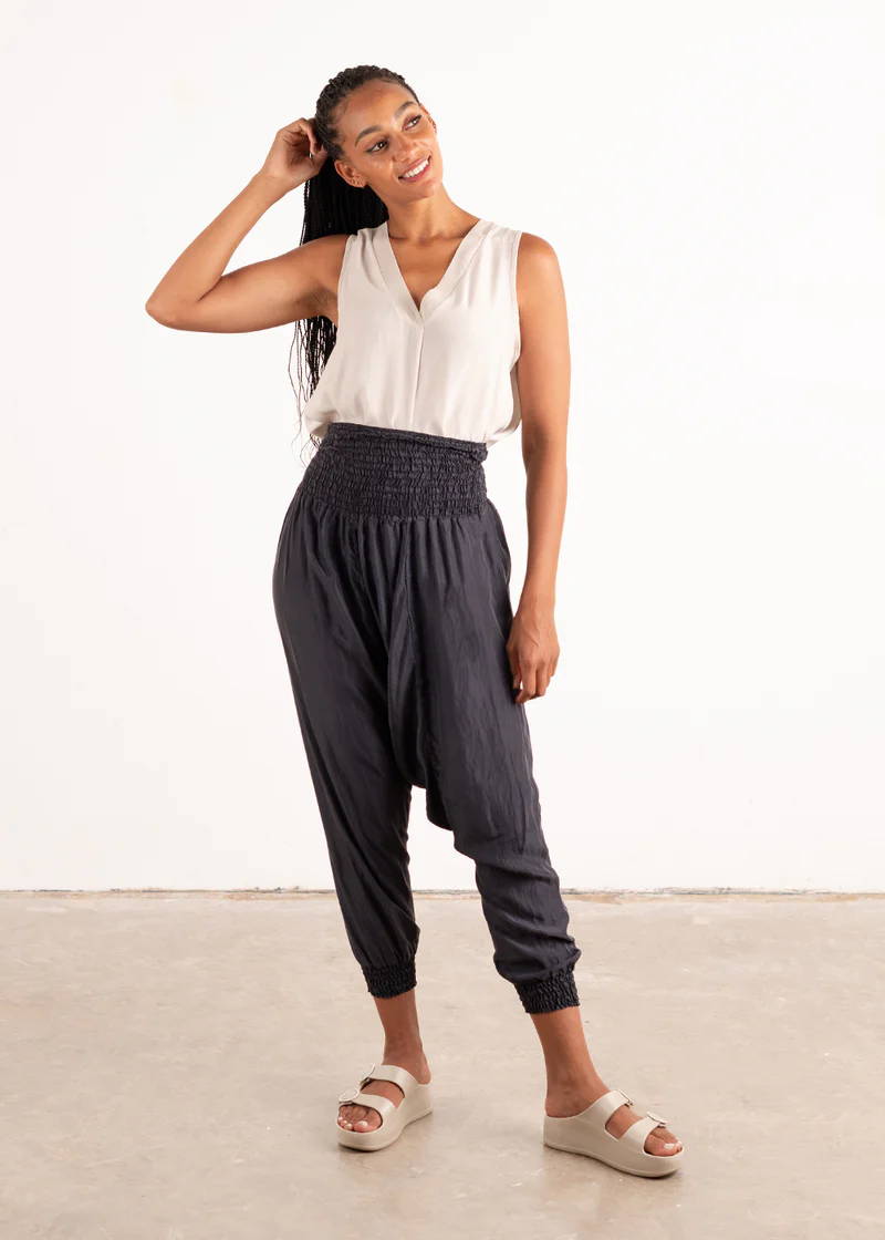 A model wearing an off white sleeveless top with dark blue silky drop-crotch trousers and off white chunky platform slides