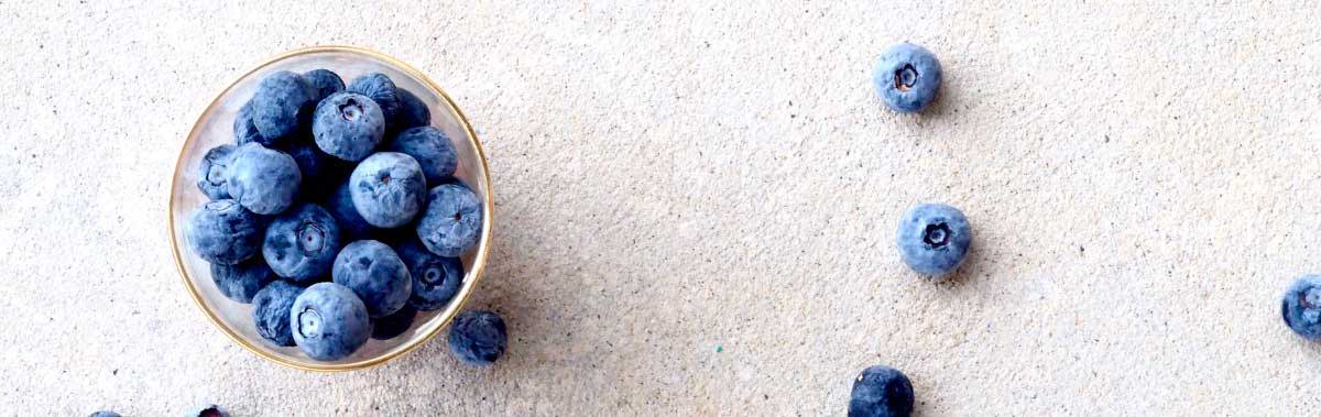 A bowl of blueberries with some blueberries on the counter