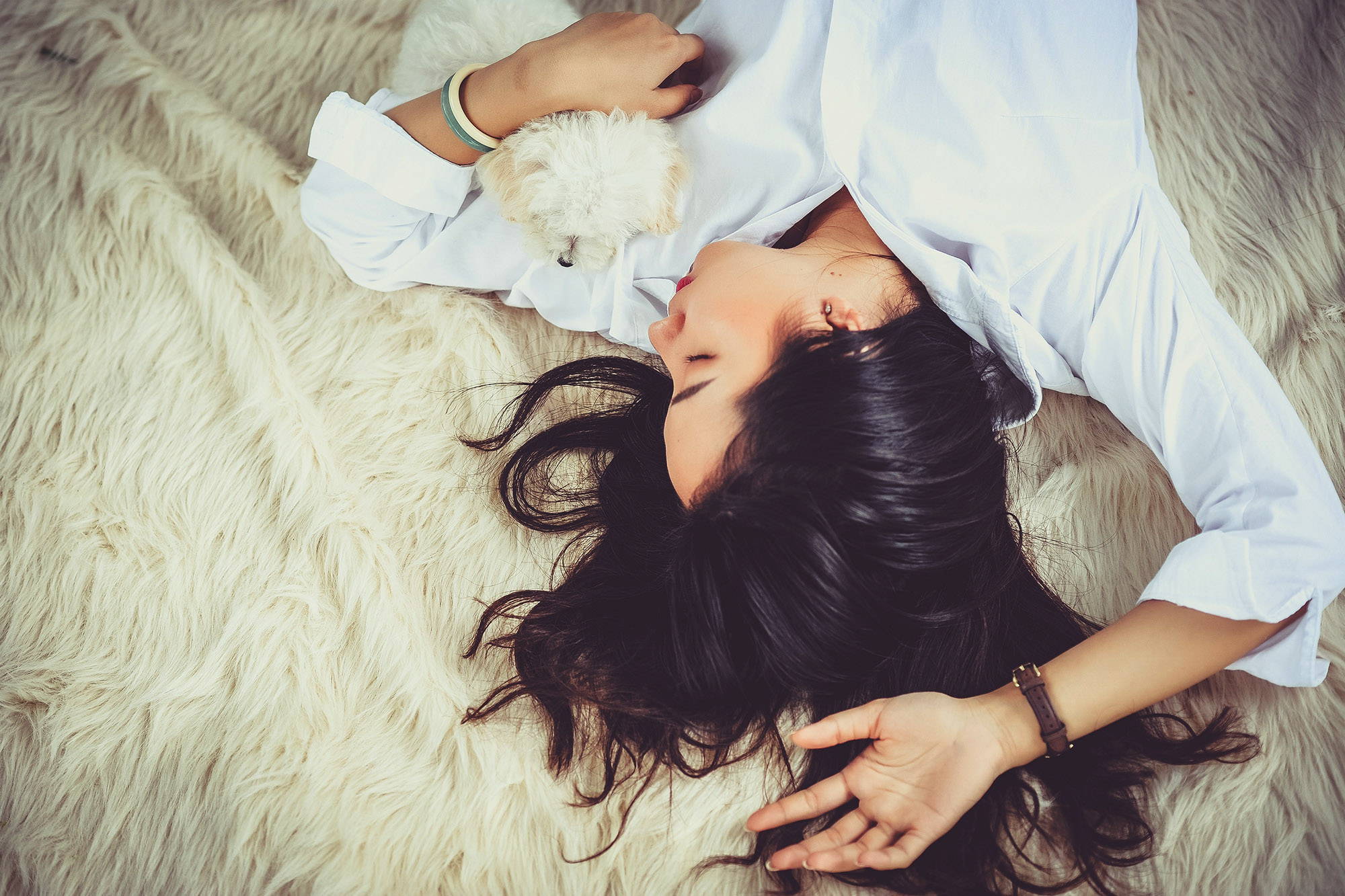 A brunette woman sleeping on her back on a fuzzy blanket with a small white dog