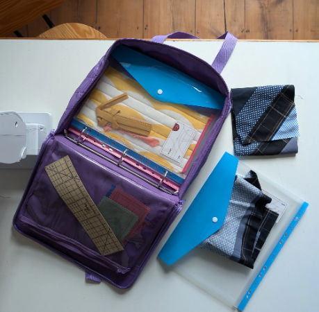 purple zipper binder bag for sewing and quilting with tools and fabrics on a white table