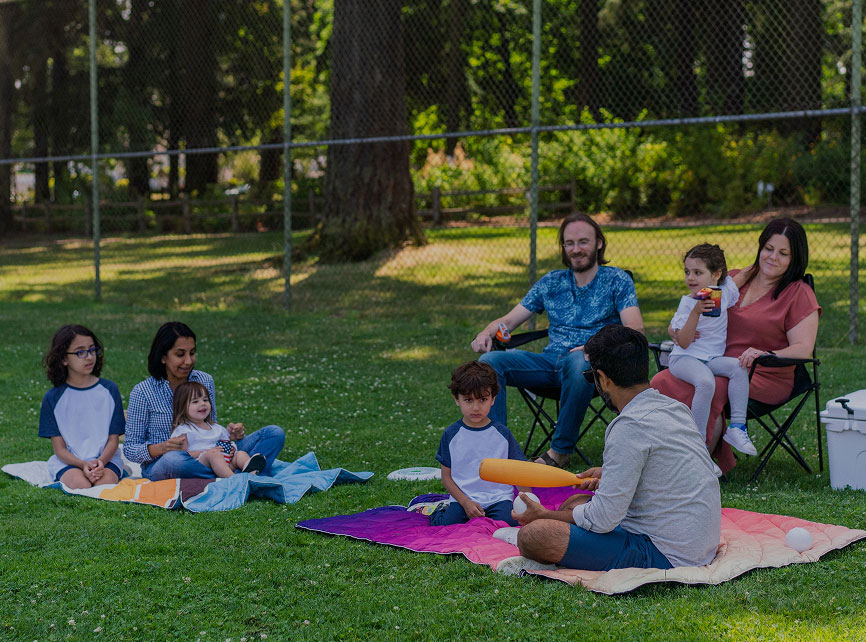Group of people sitting on blankets in a park, enjoying a picnic.