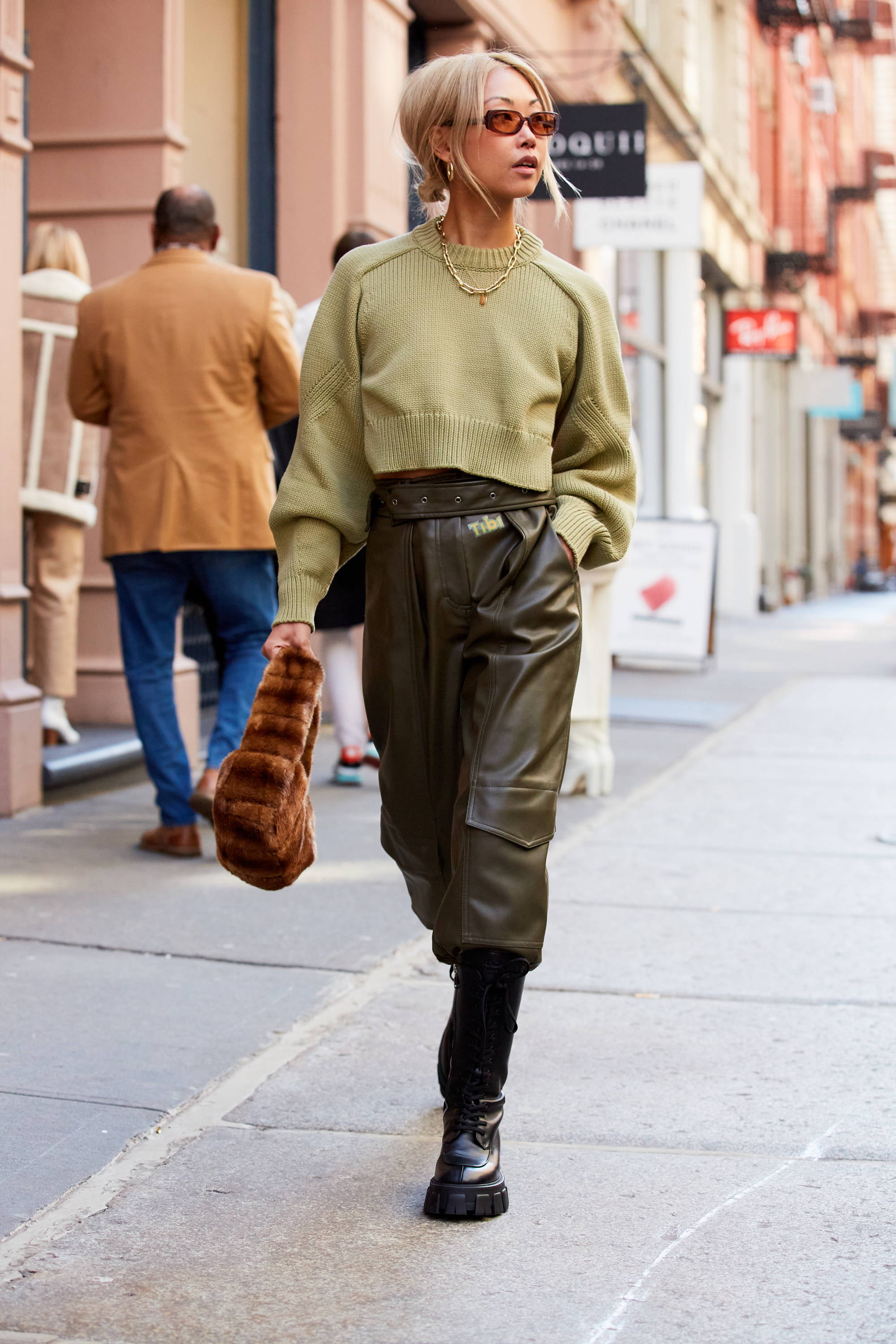 Person walking on the street, wearing a green sweater and leather pants.