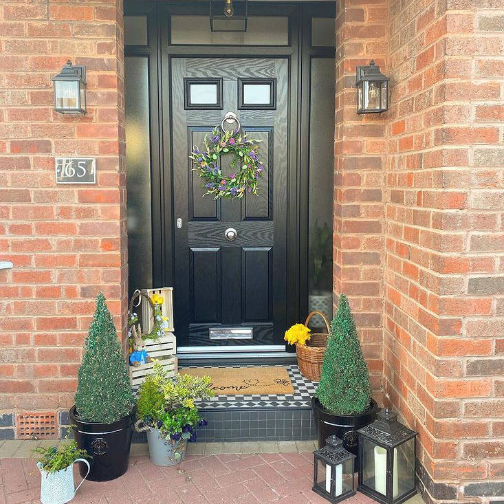 Spring doorway with wreath styled on door with outdoor lanterns and plants displayed 