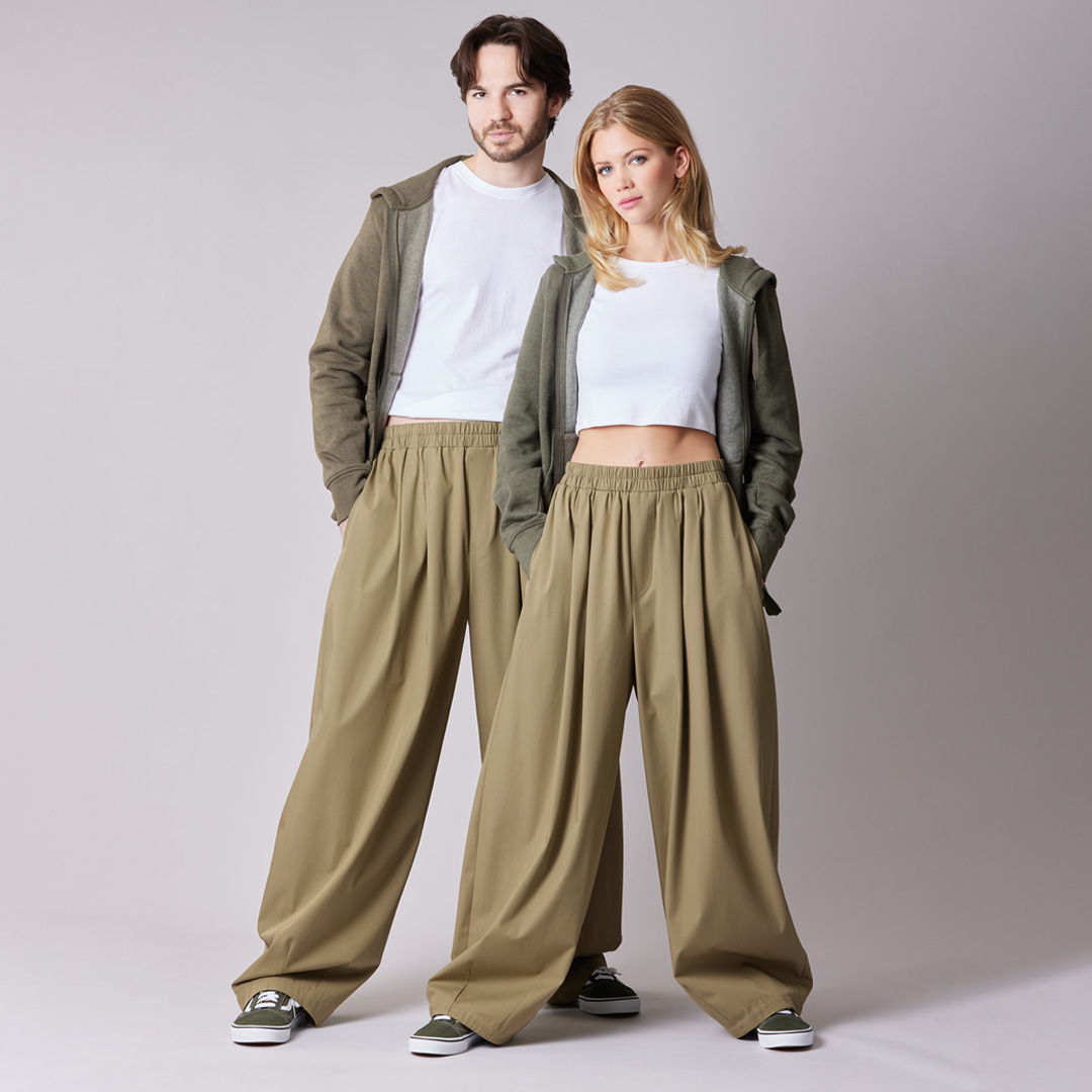 Two models wearing matching olive green outfits and relaxed trousers standing together.