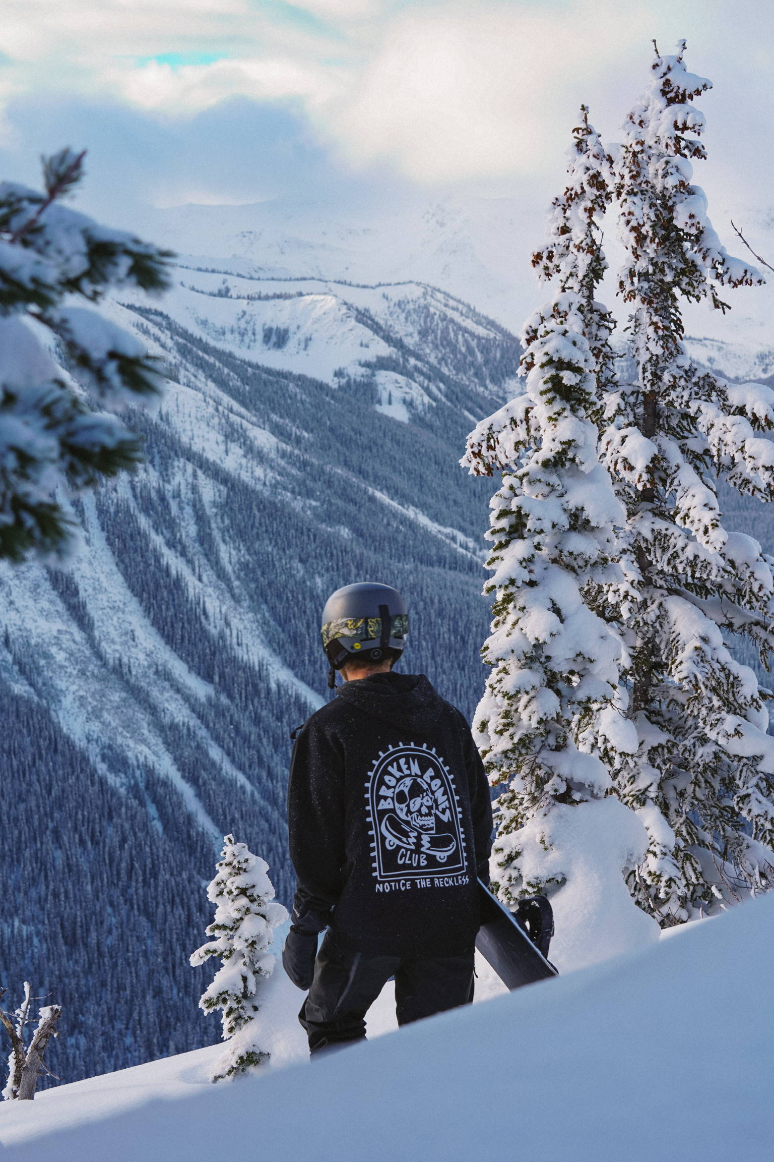 A man snowboarder with a broken bones club hoodie in the snowy mountains