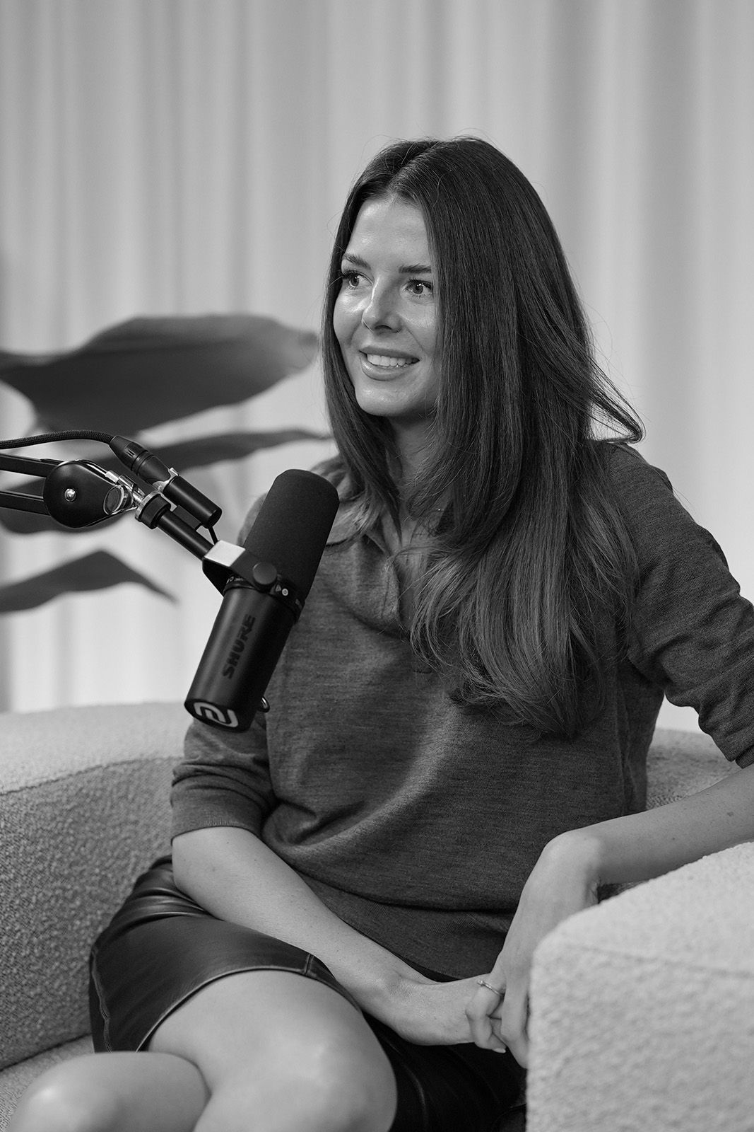 A woman with long hair sitting next to a microphone on a couch.