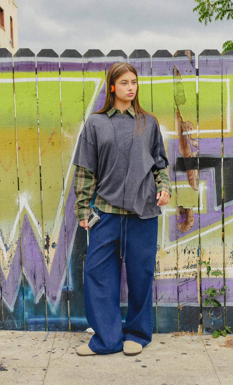 Person standing in front of a colorful graffiti wall, wearing casual oversized clothing.