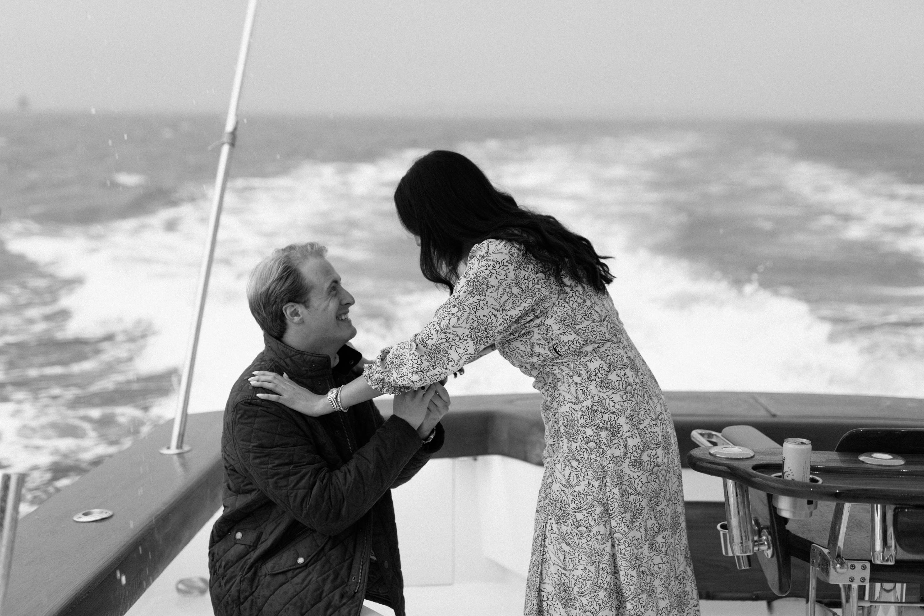 Chris kneeling to propose on the boat in black and white