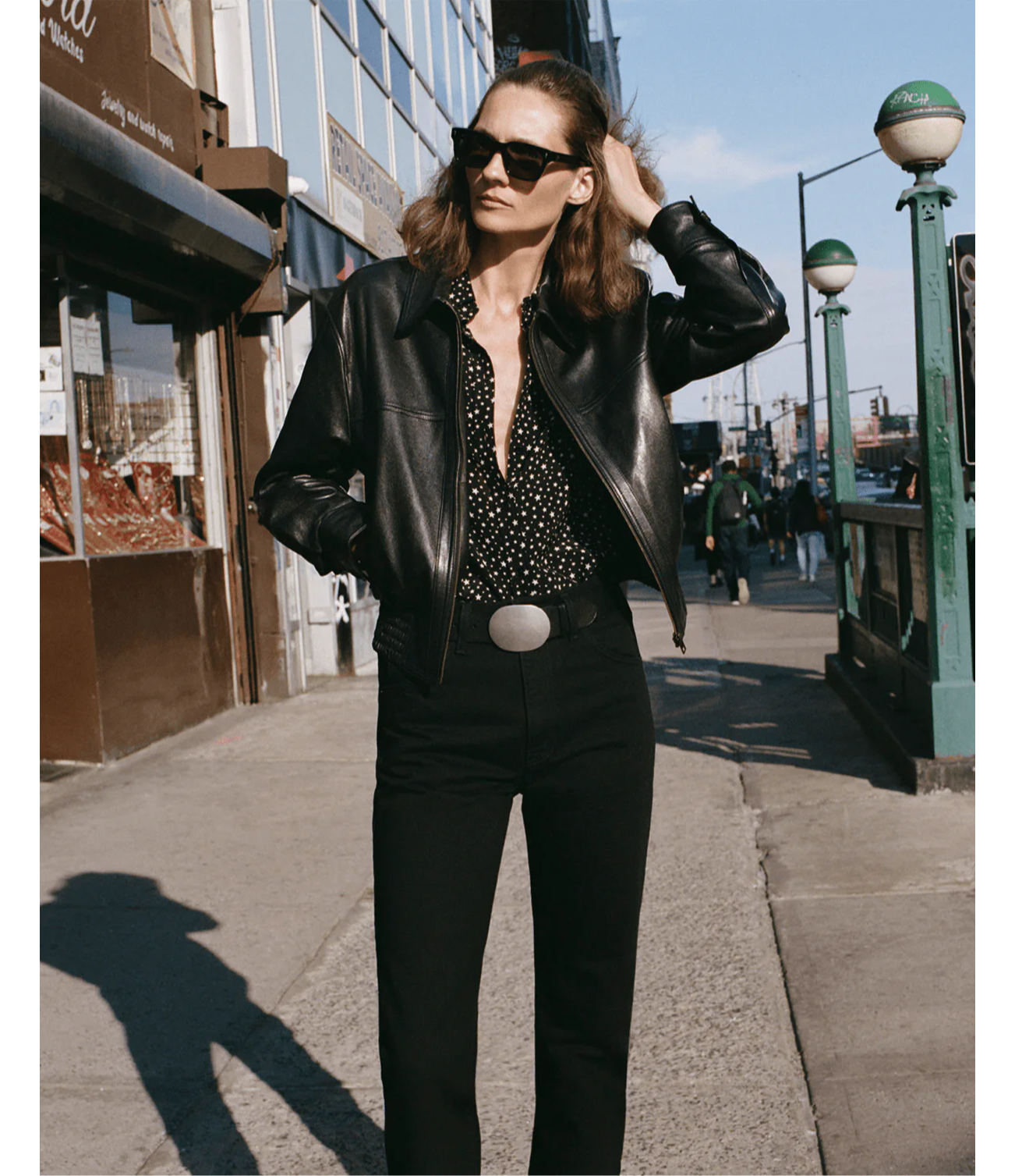 Woman in black leather jacket and sunglasses walking on a city street.